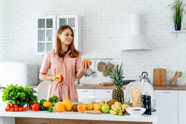 Güzel bayan elinde sebzelerle beyaz mutfakta duruyor. Yaşam tarzı sabah yemeği..
