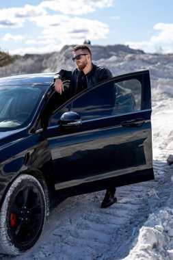 Çekici bir adam arabanın kapısını açtı. Güzel bir dağ ve gökyüzü manzarası. Siyah ve beyazın şık kombinasyonu.