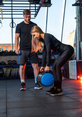 Erkek antrenör, spor salonundaki eğitmen bayana yardım ediyor. Spor giyinen atletik bayan spor yapıyor..