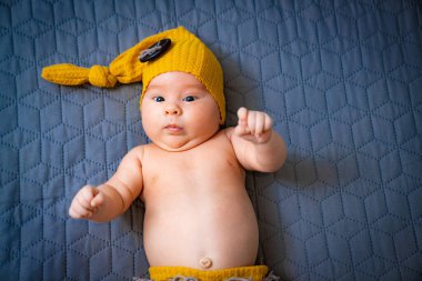 Small cute newborn baby in funny hat. Sweet pretty child lying on the blanket.