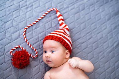 Little newborn boy with knitted hat. Cute adorable baby lying in funny red hat.