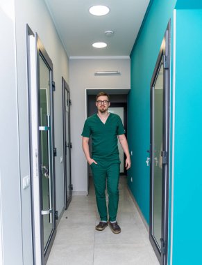 Medical specialist in uniform in modern hospital room. Confident professional doctor standing indoors.