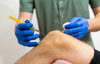 Doktor, dizine iğne yapmak için şırınga tutuyor. Diz iğnesi..