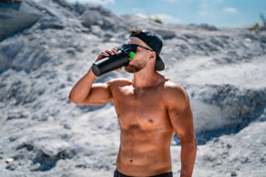 Çıplak gövdesiyle içki içen güçlü bir atletik. Formda vücutlu güçlü bir vücut geliştirici..