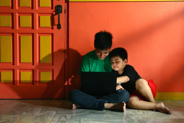 Niños asiáticos jóvenes, hermanos o hermanos, con un ordenador portátil en una sala de estar — Foto de Stock