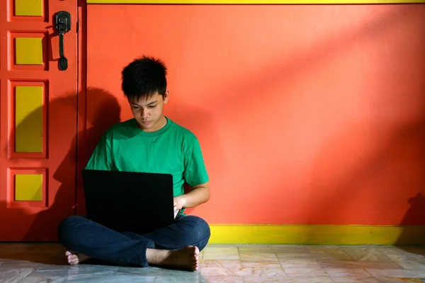 Jovem asiático adolescente com um computador portátil em uma sala de estar — Fotografia de Stock