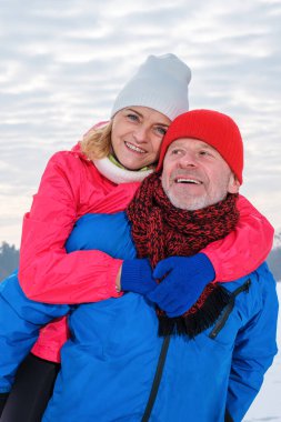 Gülümseyen kıdemli adam, olgun kadına karlı kış parkında sırt sırta veriyor.