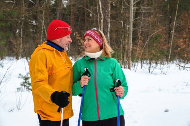 Karlı kış ormanlarında kuzeyli yürüyüş direkleriyle yürüyen yaşlı çift.