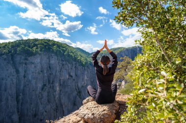Kollarını kaldırmış bir kız, dağların arkasında yoga yapıyor.