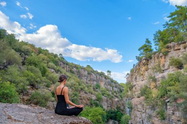 Genç kadın kayanın üstünde Padmasana duruşunu sergiliyor.