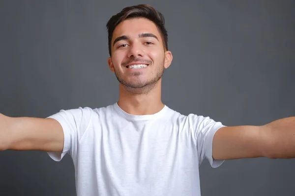Homem em uma camiseta branca fazendo selfie em um fundo cinza — Fotografia de Stock