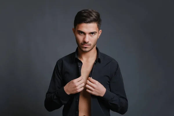 Portrait of unshaven young man buttoning up black shirt — стоковое фото
