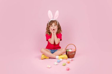 Paskalya tavşanı kulaklı kız yerde oturuyor ve gözleri yumurtayla kaplanıyor.