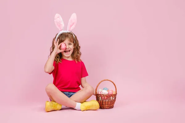 Pige i påskeharen ører sidder på gulvet og dækker øjet med æg Stock-billede