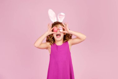 Paskalya partisinde pembe stüdyoda gözleri yumurtayla kaplayan tatlı çocuk.