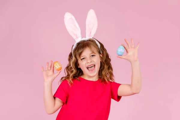 Liten flicka i påsk kanin öron ler medan håller i händerna färgglada ägg — Stockfoto