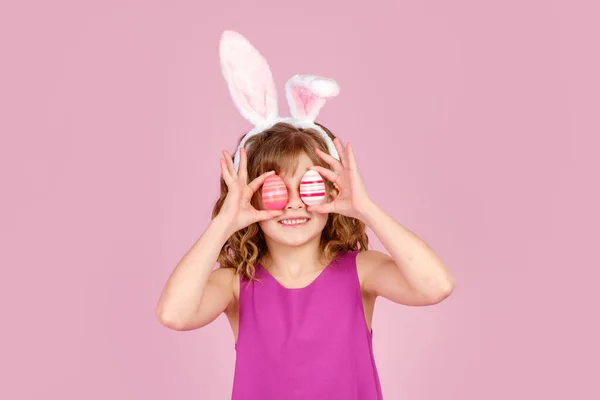 Glädjande barn täcker ögat med ägg under påskfesten i rosa studio — Stockfoto