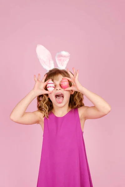 Glædeligt barn, der dækker øje med æg under påske fest i lyserødt studie Royaltyfrie stock-billeder