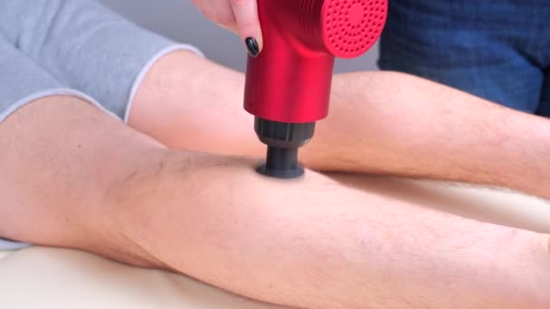 Tukang pijat wanita memijat otot betis olahragawan dengan pemijat perkusi — Stok Video