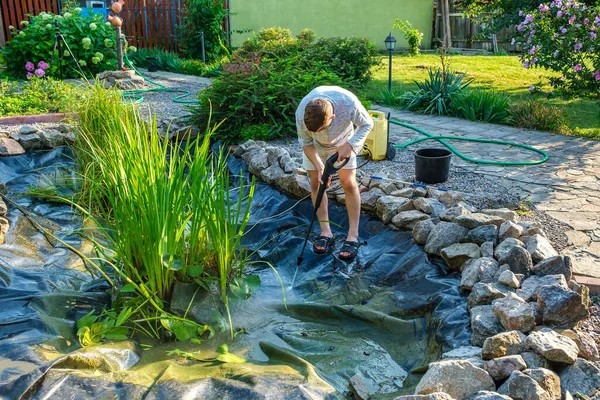 De mens reinigt tuinvijver bodem landingsnet van modder, slib en waterplanten Stockfoto
