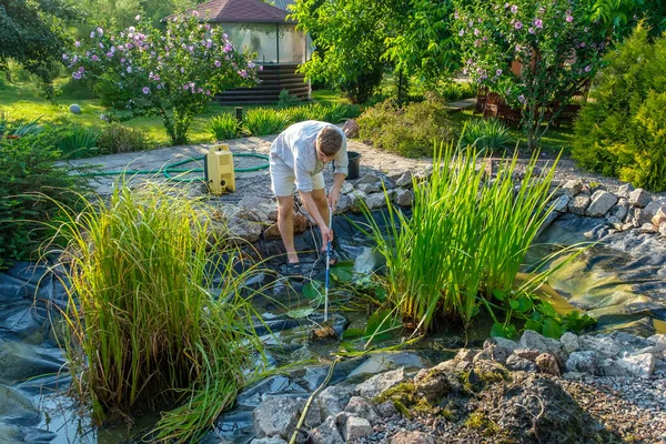 Man cleans garden pond bottom landing net from mud, sludge and water plants — Stock Photo, Image