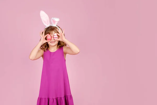 Glädjande barn täcker ögat med ägg under påskfesten i rosa studio — Stockfoto
