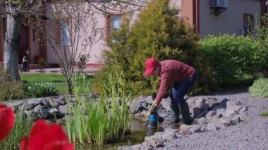 Kadın, yapay bir bahçe havuzuna su pompası bırakıyor.