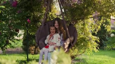 Gülümseyen ve şakacı anne-kız sallanan sandalyede iyi eğlenceler.