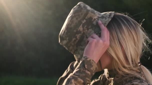 Жінка-солдат одягає камуфляжний капелюх на голову на відкритому повітрі — стокове відео