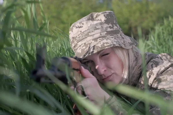 Украинская женщина-солдат, вооруженная штурмовой винтовкой, лежит в траве и целится — стоковое фото
