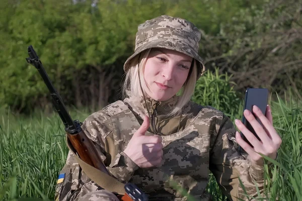 Female soldier with an assault rifle communicates with someone via video call