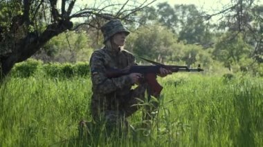 Kamuflaj üniformalı genç Ukraynalı kadın asker keşif tüfeğiyle bir muharebe bölgesinde devriye geziyor ve diz çökerken nişan alıyor. Ormanda silahlı cesur bir vatansever kadın.