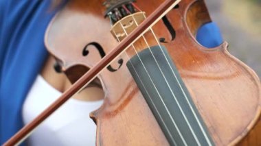 Unrecognizable woman musician playing performing violin outdoors. Bow close-up, macro shooting, no face, defocused background. 