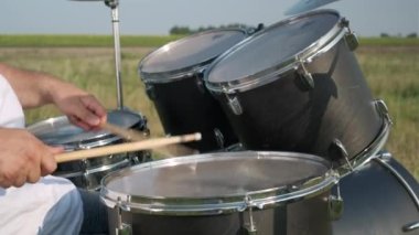 Hands of an unidentified professional drummer, emotionally playing a drum roll on the drum kit outdoors on a sunny summer day in the middle of green grass