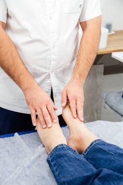 Bir osteopat bir kadının ayaklarına parmaklarıyla dokunur, masaj koltuğunda tedavi edici bir test uygular.