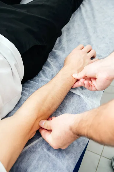 Un fisioterapeuta tratando a un paciente. Osteópata sostiene una mano de hombre —  Fotos de Stock