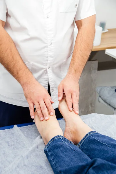 Un osteopat atinge picioarele unei femei cu degetele, efectuează un test terapeutic pe o canapea de masaj — Fotografie, imagine de stoc