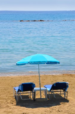 Deniz üstünde şemsiye altında mavi şezlonglar
