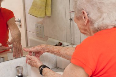 Yaşlı kadın ellerini banyoda sıvı sabunla yıkıyor.