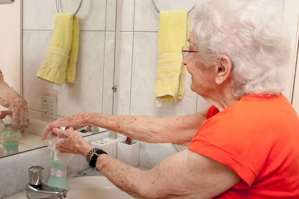 Elderly Lady Washing her Hands with Liquid Soap in the Bathroom