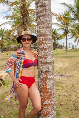Caraiva, Bahia, Brezilya 'da plajın yakınındaki bir palmiye ağacına yaslanmış bir kadın.