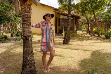 Caraiva, Bahia, Brezilya 'da plajın yakınındaki bir palmiye ağacına yaslanmış bir kadın.