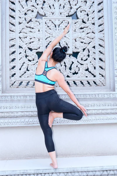 Young Asian woman is exercising with difficult yoga exercises in the morning in front of the temple yard to have good health to start an effective working day.