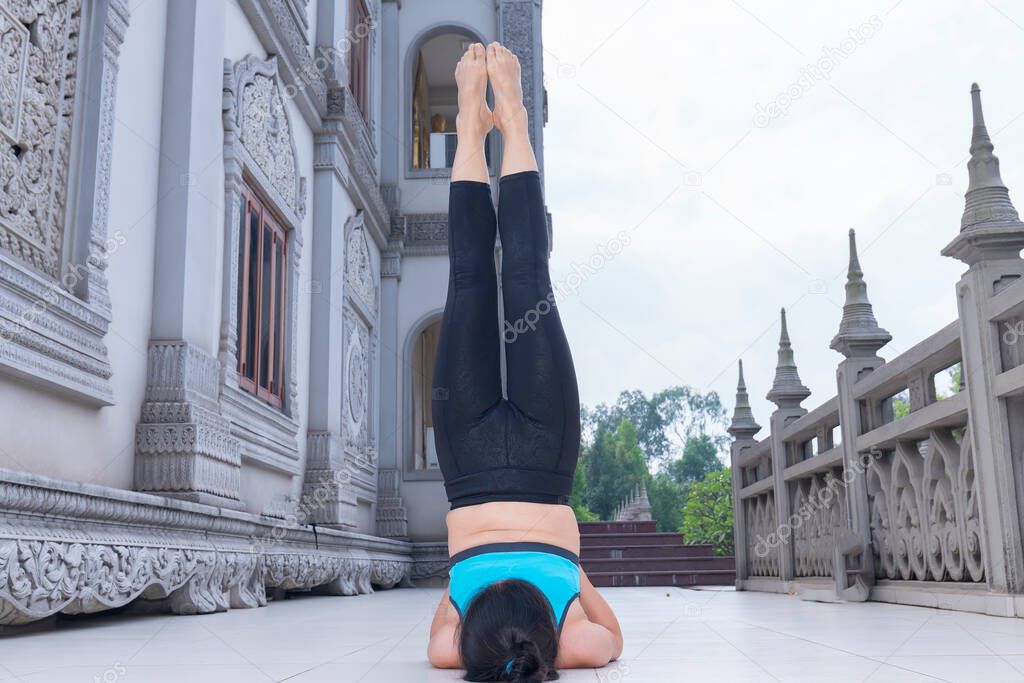 Young Asian woman is exercising with difficult yoga exercises in the morning in front of the temple yard to have good health to start an effective working day.