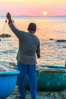 Gün batımında güzel sahilde ağları boşaltan balıkçı silueti. Yarın sabah Vietnam 'ın merkez sahillerinde başarılı bir yelken açmaya hazırlanmak için günlük işler.