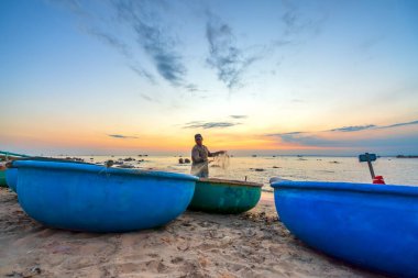 Mui Ne, Vietnam - 24 Ocak 2022: Gün batımında balıkçılar ağlarına takılıp ertesi sabah Mui Ne, Vietnam 'da denize açılmaya hazırlanırken sepet tekne rıhtımının manzarası