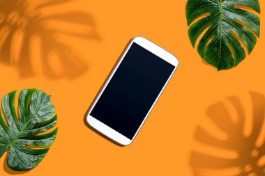 Tropikal canavar yaprakları ve gölgesi olan akıllı telefon.