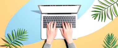 Tropikal yaprakları olan bir dizüstü bilgisayar kullanan kişi