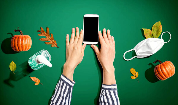 Smartphone with mask and sanitizer bottle in Autumn