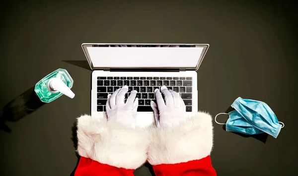 Santa Claus pomocí notebooku s maskou a dezinfekční láhví — Stock fotografie